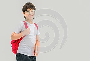 Asian child boy in glasses and red backpack holding book in his hand