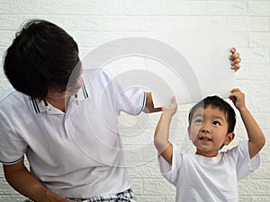 Asian child boy holding white board on head with dad with happy smiling face.