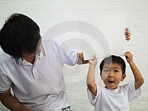 Asian child boy holding white board on head with dad with happy smiling face.