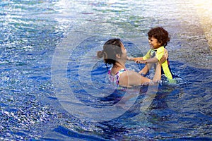 Asian child boy learn swimming in a swimming pool with mom. - Sunset filter effect