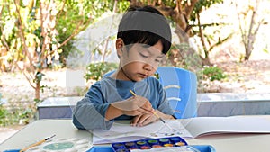 Asian child boy painting by watercolor and brush at home with happy relaxing face.