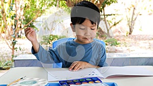 Asian child boy painting by watercolor and brush at home with happy relaxing face.
