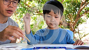 Asian child boy painting by watercolor and brush together with father at home. Dad and cute son in happy moment.