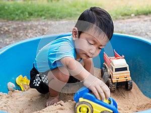 Asian child boy playing car toy in sandbox outdoor in rural nature background with smiling face.