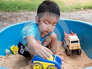 Asian child boy playing car toy in sandbox outdoor in rural nature background with smiling face.