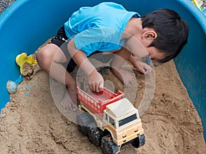 Asian child boy playing car toy in sandbox outdoor with smiling face.