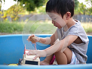 Asian child boy playing sand and truck toy in sandbox outdoor in rural nature background with happy face.