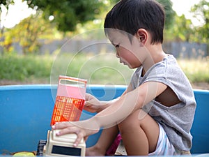 Asian child boy playing sand and truck toy in sandbox outdoor in rural nature background with happy face.