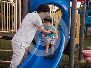 Asian child boy playing slider in playground together with dad in happy family time.