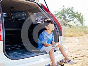 Asian child boy sitting and thinking with upset unhappy face in rear of white car.