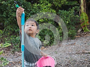 Asian child boy turning sprinkler with serious face in garden at home.