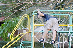 An Asian child climbs up an alpine grid in a park on a playground on a hot summer day