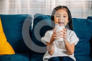 Asian child enjoys a glass of milk on the sofa their happiness and innocence