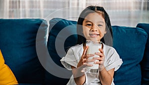 Asian child enjoys a glass of milk on the sofa their happiness and innocence