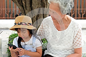 Asian child girl is addictive play mobile phone addicted to the game, have an elderly grandmother sit with caring concern