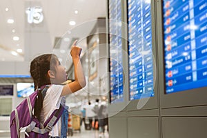 Asian child girl with backpack checking her flight at information board in international airport terminal