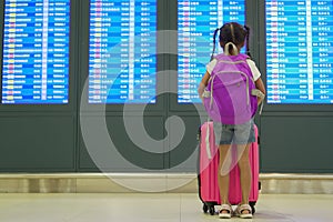 Asian child girl with backpack checking her flight at information board in international airport terminal