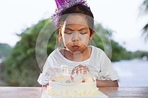 Asian child girl celebrating birthday and blowing candles on birthday cake in the party