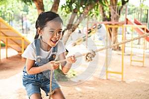 Asian child girl is climbing a wooden wall with a rope in the playground with fun and strong