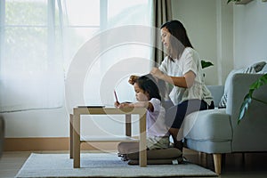 Asian child girl doing homework and mother is combing her hair