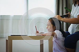 Asian child girl doing homework and mother is combing her hair