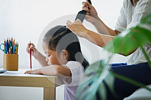 Asian child girl doing homework and mother is combing her hair