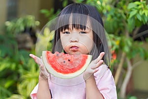 Asian child girl eating and biting a piece of watermelon.