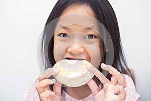 Asian child girl is eating a cream donut. She is enjoying eating unhealthy food