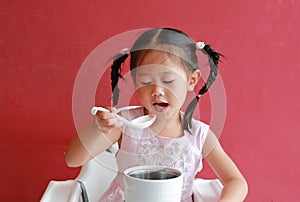 Asian child girl eating pork bone soup on high chair against red wall background at chinese restaurant
