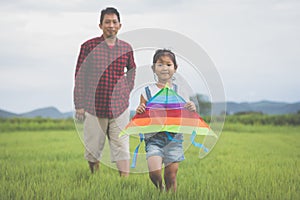 Asian child girl and father with a kite running and happy on meadow in summer in nature