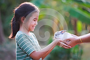 Asian child girl getting adorable bunny from her mother hand and she  playing and caring cute little rabbit holland lop