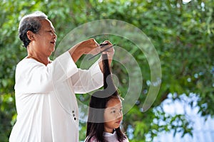 Asian child girl getting haircut by grandmother at home