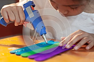 Asian child girl glueing colored ice cream sticks by hot melt electrical glue gun.