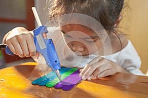 Asian child girl glueing colored ice cream sticks by hot melt electrical glue gun.