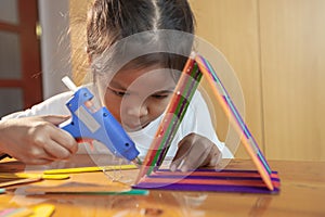 Asian child girl glueing colored ice cream sticks by hot melt electrical glue gun.