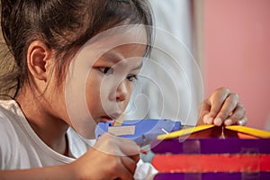 Asian child girl glueing colored ice cream sticks by hot melt electrical glue gun.