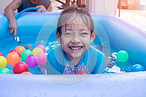 Asian Child Girl Having Fun In Garden Paddling Pool with father fill wather in background