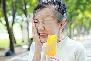 Asian child girl having hypersensitive teeth eating ice-pop,feel painful,female teenage have sensitive teeth with ice-lolly,sad