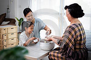 Asian child girl and her mother pouring water on hands of elder senior or respected grandparents for celebrate Songkran in new