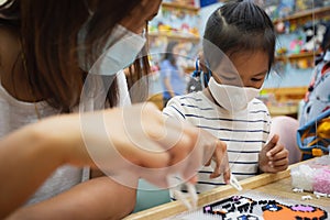 Asian child girl and her mother wearing protection mask making fusible beads thermo mosaic in pegboard that is a toy to develops
