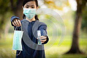 Asian child girl hold a protective mask and bottle of alcohol antiseptic gel,equipment for disinfection,pandemic of Covid-19,