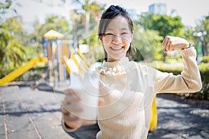 Asian child girl holding a glass of milk,showing her bicep to tell she is strong,healthy female teenage drink fresh milk,looking