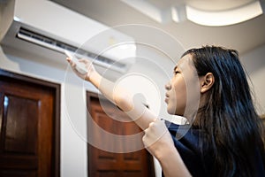 Asian child girl holding a remote control,turn on the air conditioner,adjust the temperature to cool to cool down the heat,feels photo