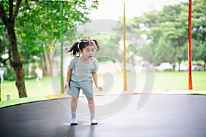 Asian child girl is jumping on trampoline on playground background. Happy laughing kid outdoors in the yard on summer vacation.