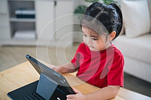 Asian child girl looking using and touch tablet display screen. Baby smiling funny time to use tablet. Too much screen time. Cute