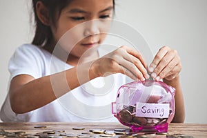 Asian child girl putting money into piggy bank to save money for the future