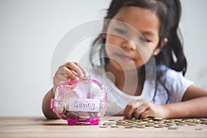 Asian child girl putting money into piggy bank to save money for the future