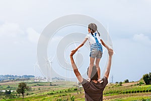 Asian child girl riding on father`s shoulders in the wind turbine field