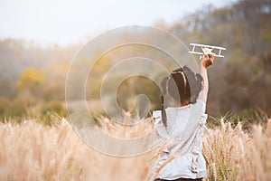 Asian child girl running and playing with toy wooden airplane in the barley field at sunset time with fun