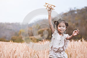 Asian child girl running and playing with toy wooden airplane in the barley field at sunset time with fun